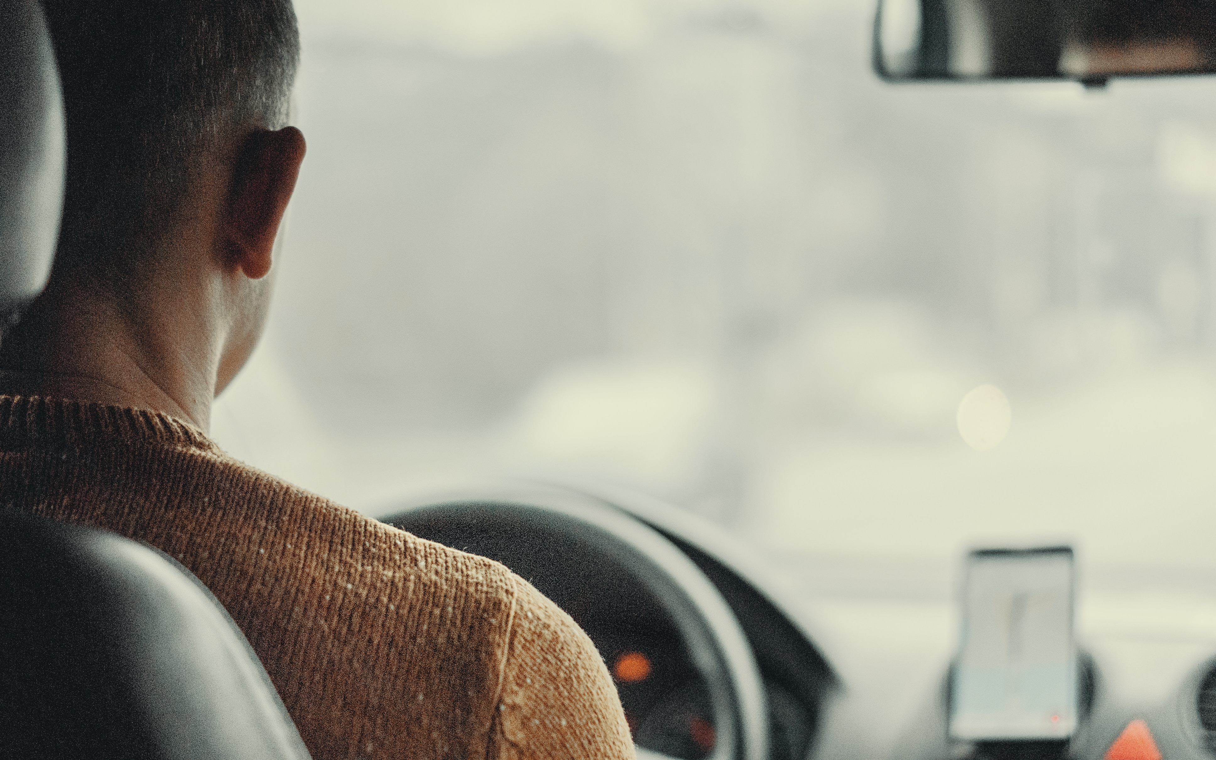 A man driving a car for a ride service app with his phone mounted on the dash of his car to use as GPS.